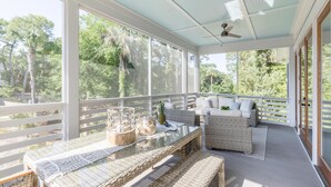A covered outdoor area with wicker furniture, a glass table, and a ceiling fan.