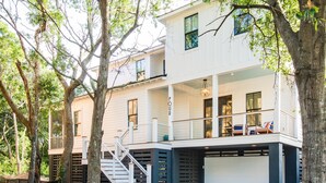 Une maison à deux étages avec un garage fermé, un escalier menant à l’étage supérieur et un grand arbre au premier plan.