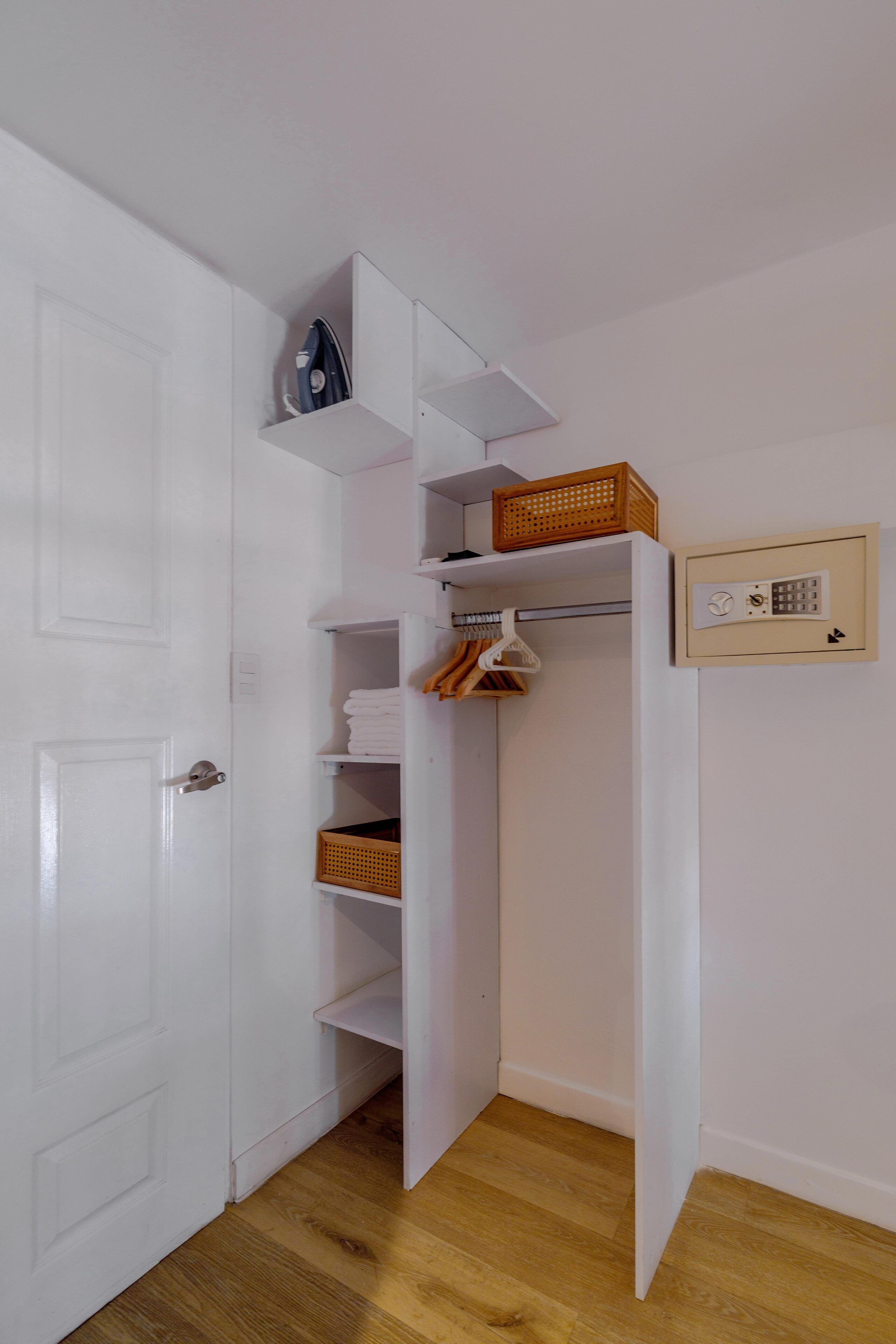 A white closet with shelves, a hanging rack, and a small wall-mounted electrical box.
