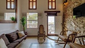 A living room with a brown sofa, a rocking chair, a potted plant, and a stone wall. - 2 BR Walled City Loft Jacuzzi - Downtown (Cartagena de Indias)