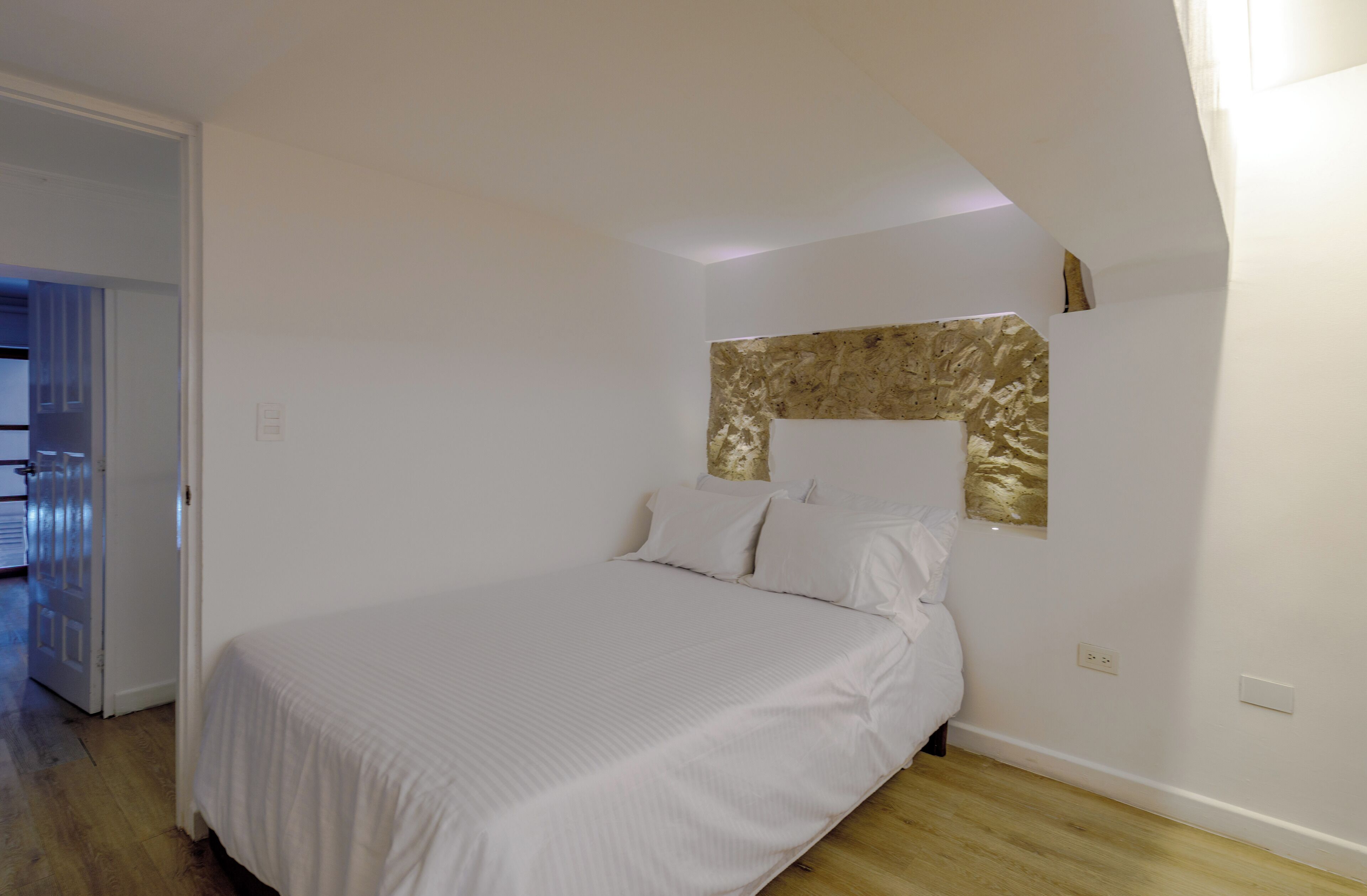 Un dormitorio con una cama, piso de madera y pared blanca con textura decorativa.