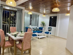 A dining area with a table set for four, surrounded by pink chairs, a blue sofa, and a white armchair.