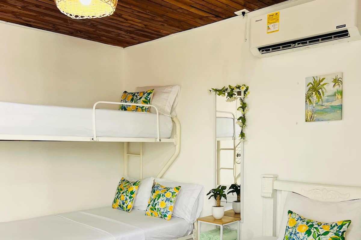 A room with bunk beds, a bedside table with a plant, a wall-mounted air conditioner, and a hanging light fixture.