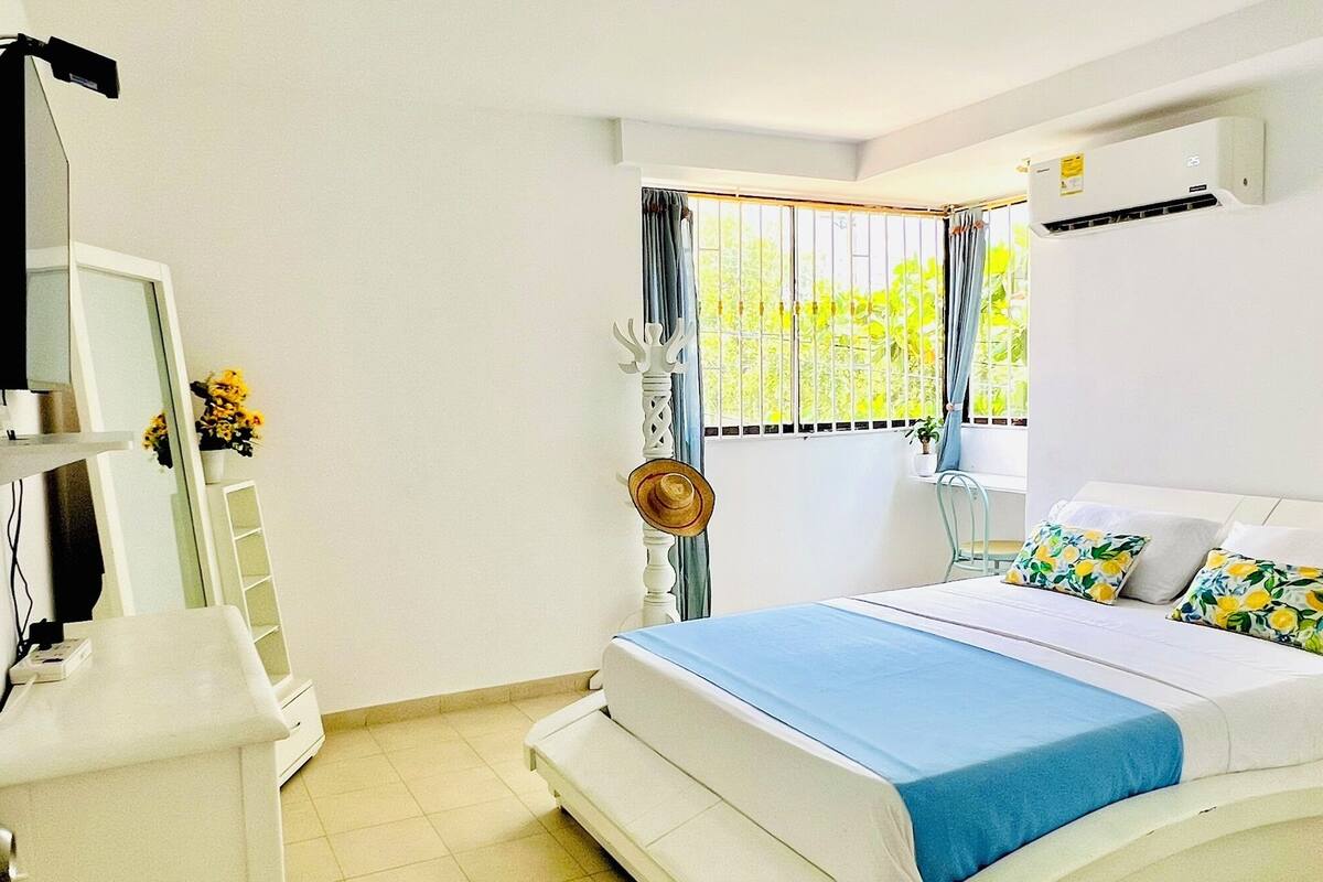 A bedroom with a bed, a desk, a mirror, and a window with curtains.