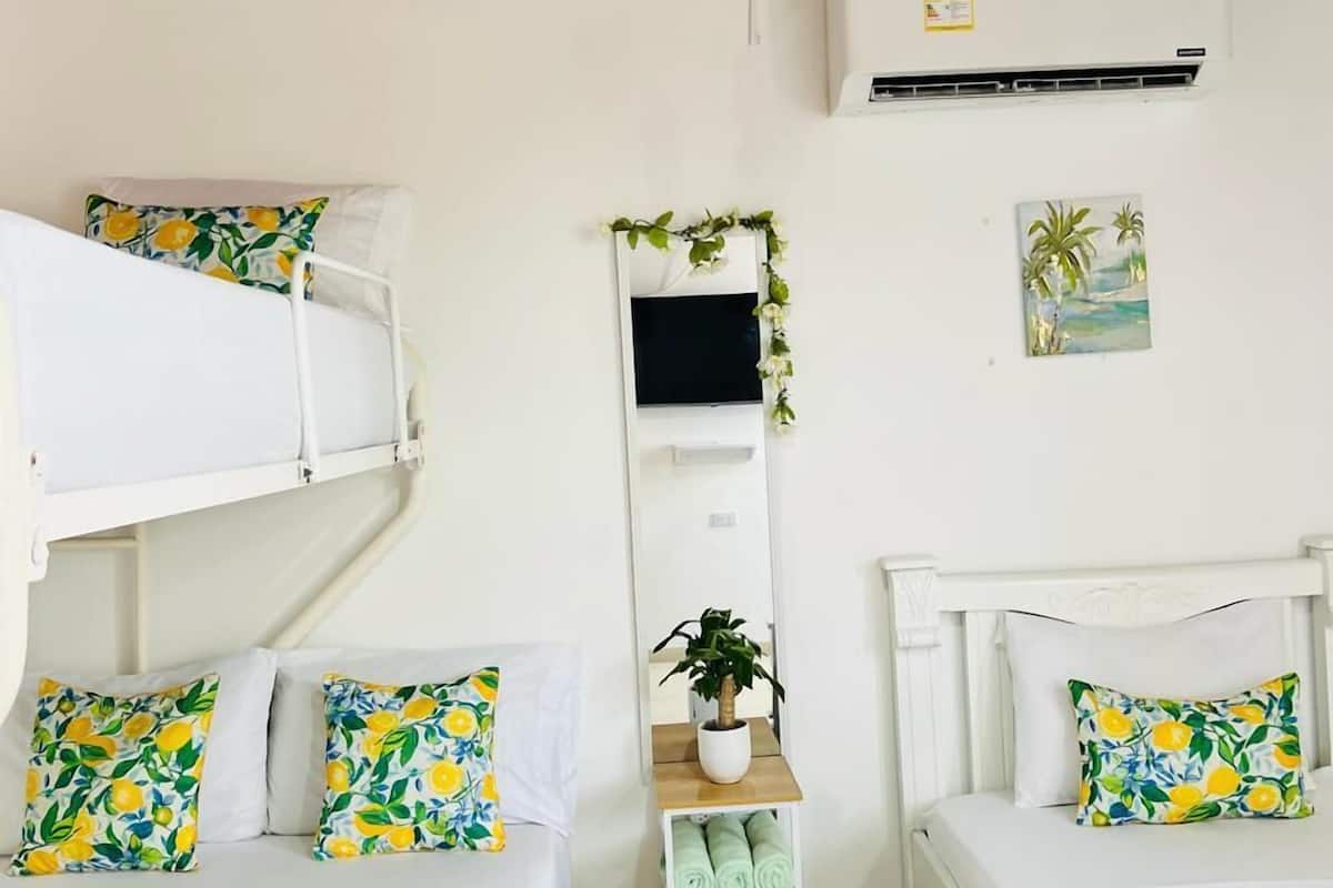 A room with two beds, a small table with a plant, a wall-mounted TV, and a painting.