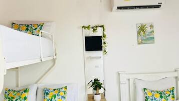 Una habitación con dos camas, una mesita con una planta, un televisor montado en la pared y un cuadro.