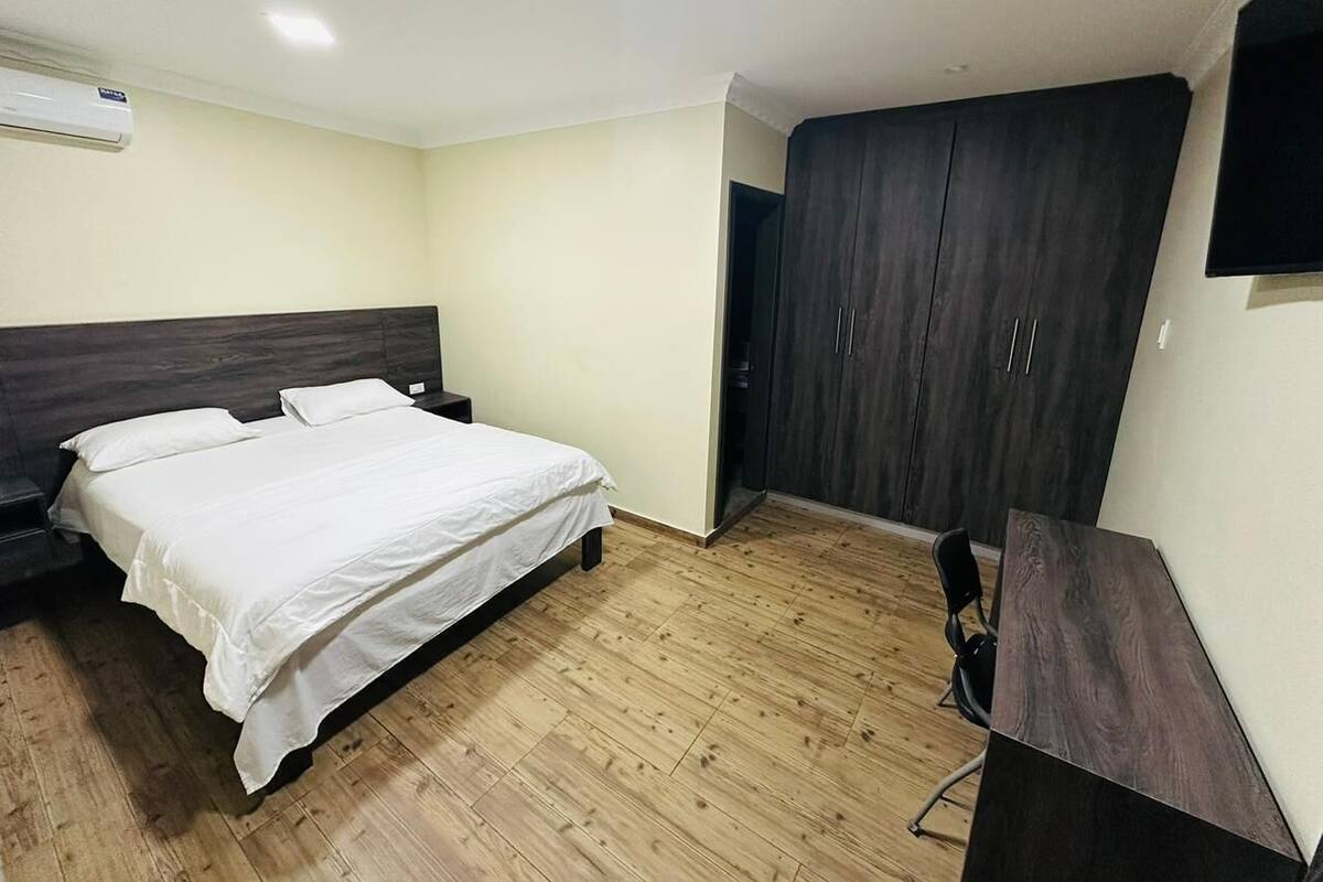 Een slaapkamer met een bed, een garderobe, een bureau en een airconditioner.