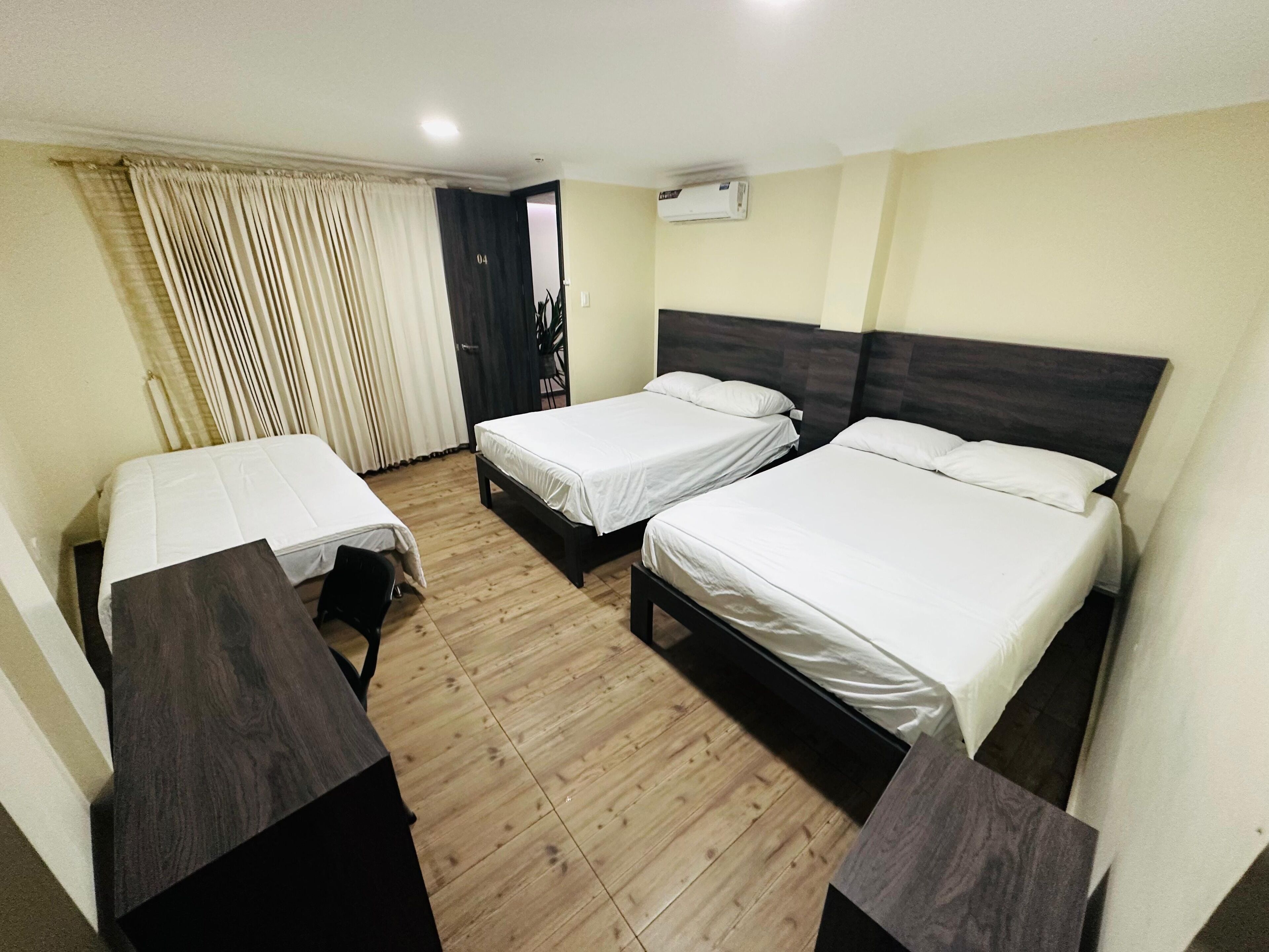 Habitación de hotel con dos camas individuales, piso de madera, cabecera oscura y ventana con cortinas.