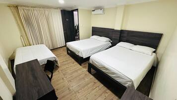 Habitación de hotel con dos camas individuales, piso de madera, cabecera oscura y ventana con cortinas.