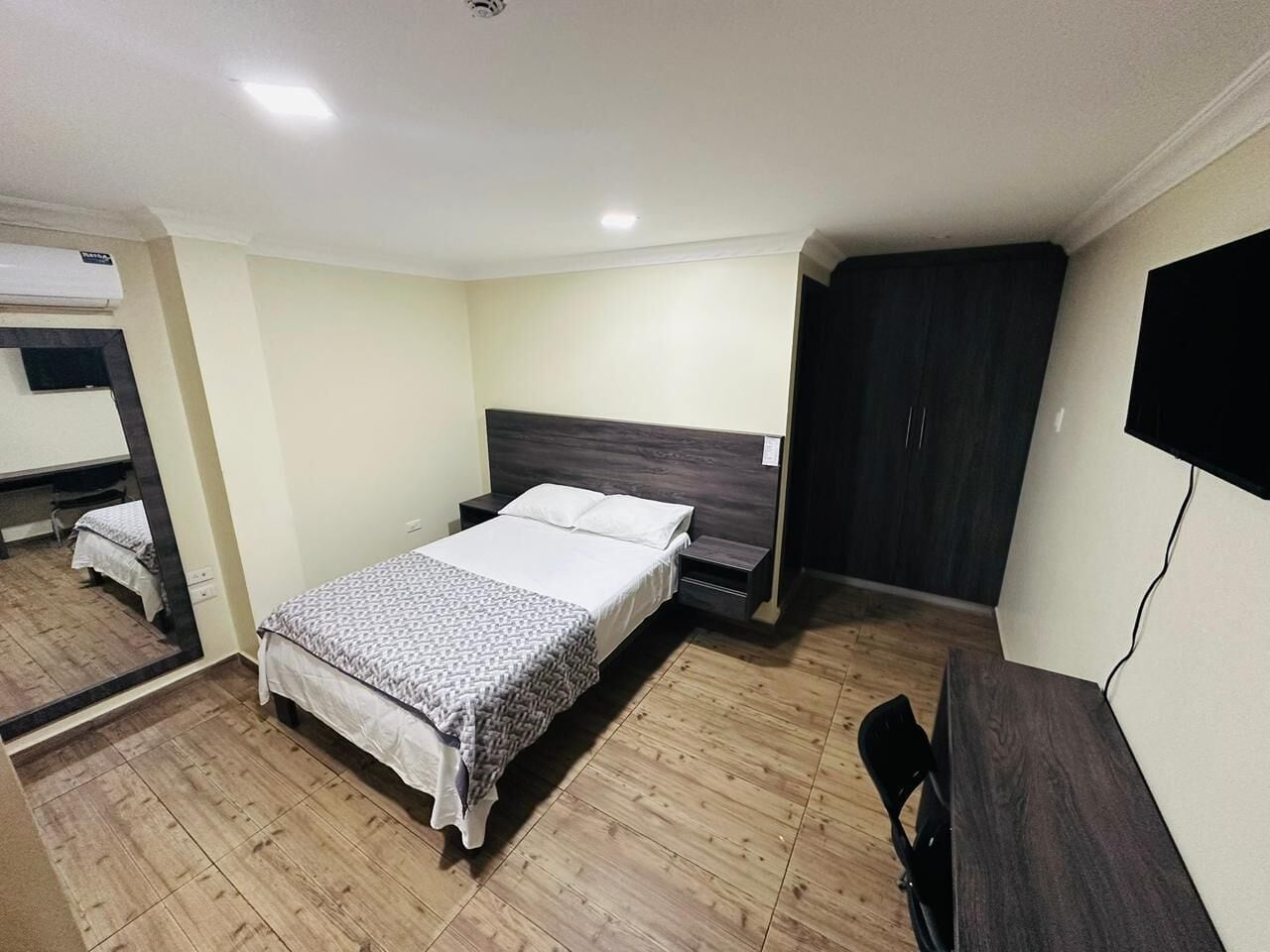 A bedroom with a bed, a wardrobe, a mirror, and a TV.