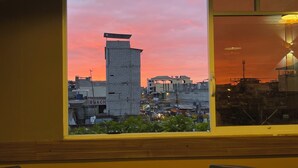 A room with a large window overlooking a cityscape at sunset, a round table, and a chair. - Hotel Vivanco's (Huaquillas)