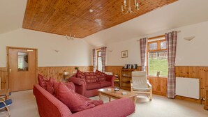 A cozy living room with a wooden ceiling, a red sofa, a wooden coffee table, and a window with curtains.