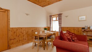 A cozy room with a wooden ceiling, a dining table with chairs, a red sofa, and a window with curtains.