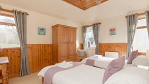 A bedroom with two beds, wooden wardrobe, and a window with curtains.