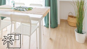 A bright room with a wooden table, white chairs, a TV on a shelf, and green curtains.