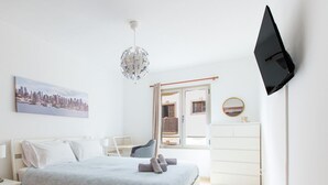 Un dormitorio moderno con cama, escritorio, silla, cómoda y televisor montado en la pared.