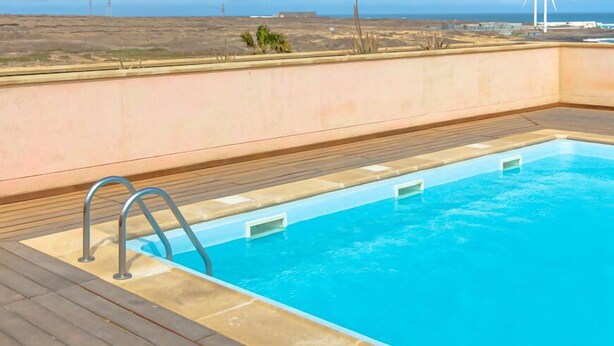 Una piscina en la azotea con vistas despejadas al océano y aerogeneradores a lo lejos.