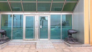 Fachada de un edificio con puertas de vidrio, una placa con el nombre y dos esculturas de piedra.