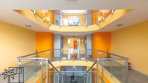 Un interior de varios niveles con barandas de vidrio, una escalera central y paredes anaranjadas.