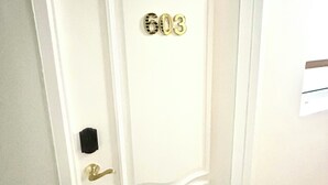 Una puerta blanca con el número 603, un picaporte de latón y un objeto negro pequeño en el marco de la puerta.