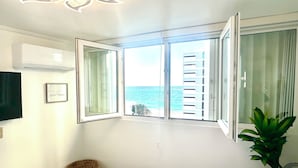Un dormitorio con cama, ventana con vista al mar, ventilador de techo y aire acondicionado de pared.