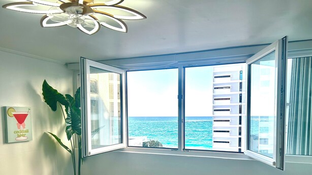 Una habitación con un amplio ventanal con vista al mar, un ventilador de techo y aire acondicionado instalado en la pared.