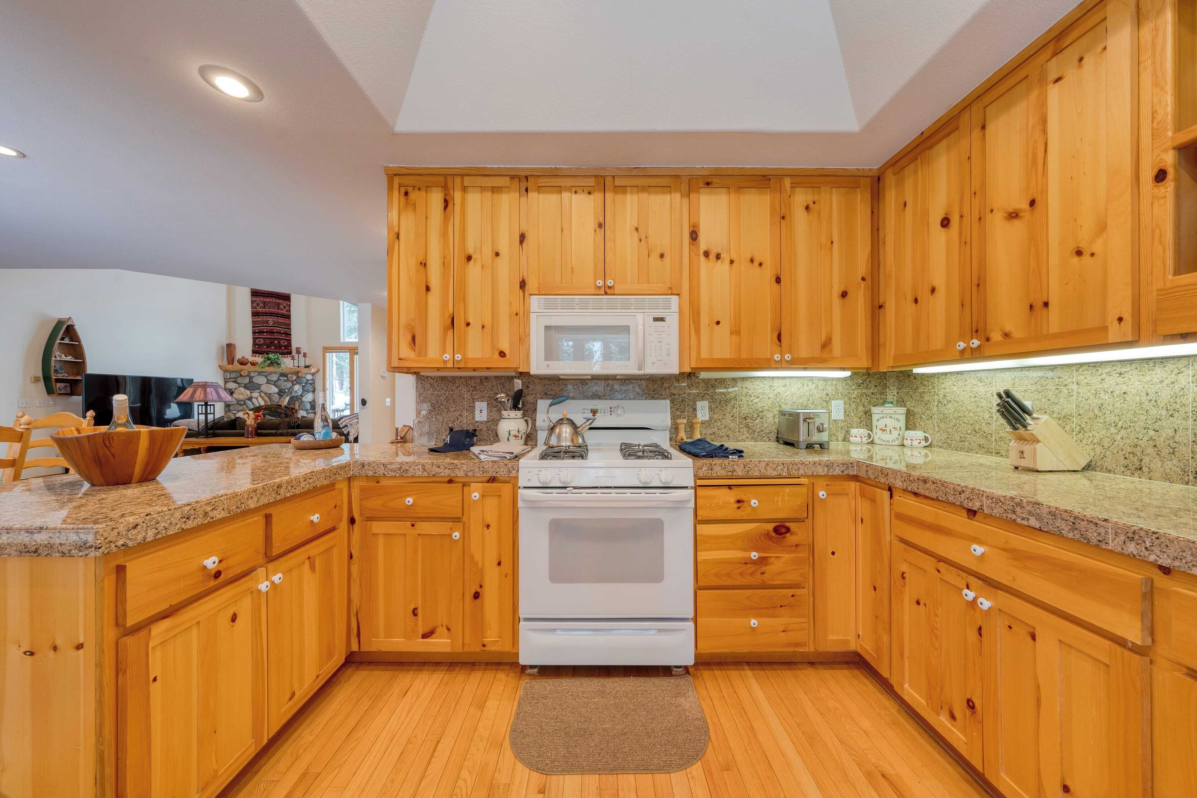 A kitchen with wooden cabinets, a white stove, granite countertops, and a microwave.