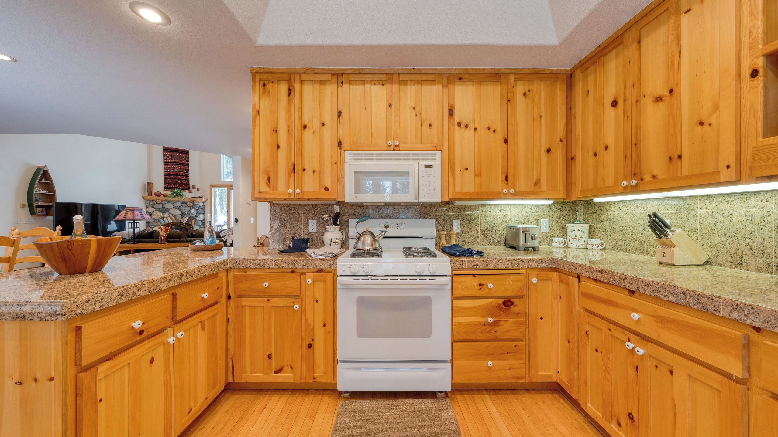 A kitchen with wooden cabinets, a microwave, a stove, granite countertops, and a stone fireplace.