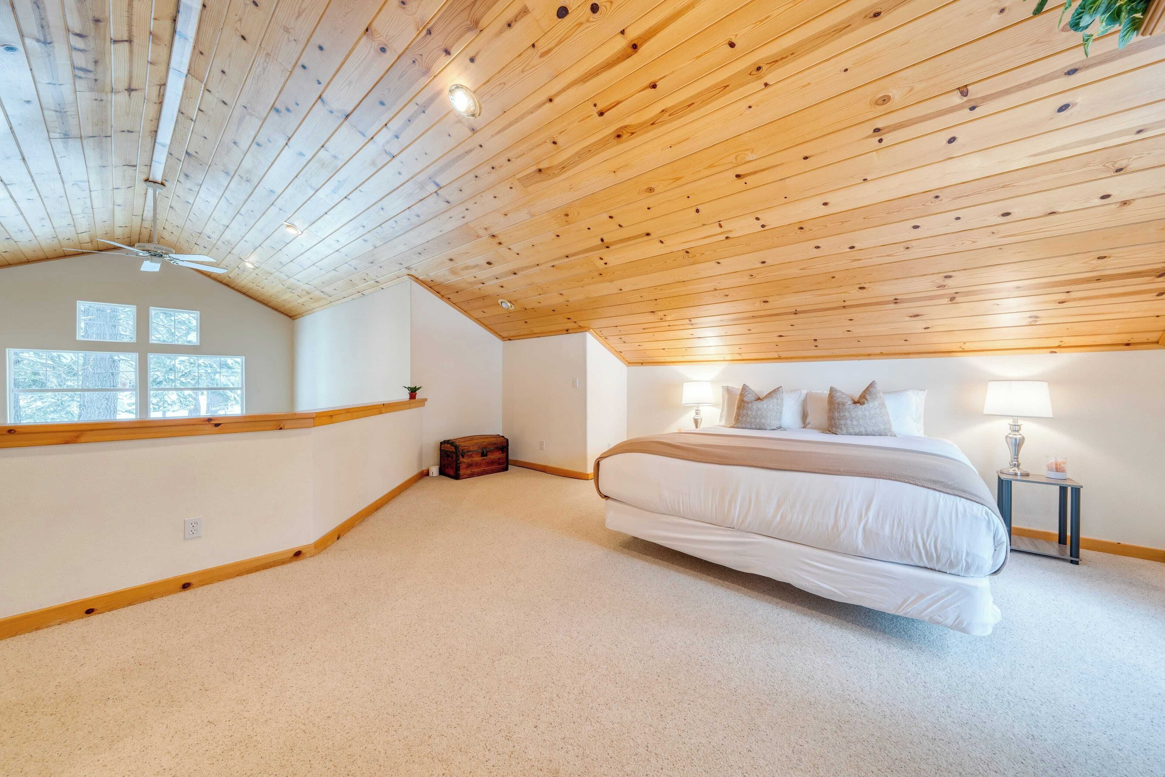 A bedroom with a sloped ceiling, a large bed, bedside lamps, and a window.