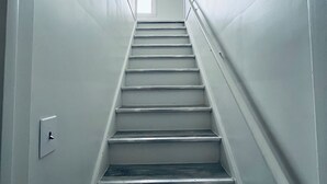 A narrow, straight staircase with white walls and a door at the top. - Large Yard Ferndale Home near Motor City Detroit. Pet-Friendly! (Ferndale)