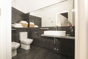 A modern bathroom with dark tiles, a white sink, a toilet, and a bidet. - MAR ABIERTO B - Charming loft with shared pool and free Wi-Fi (Sanlúcar de Barrameda)