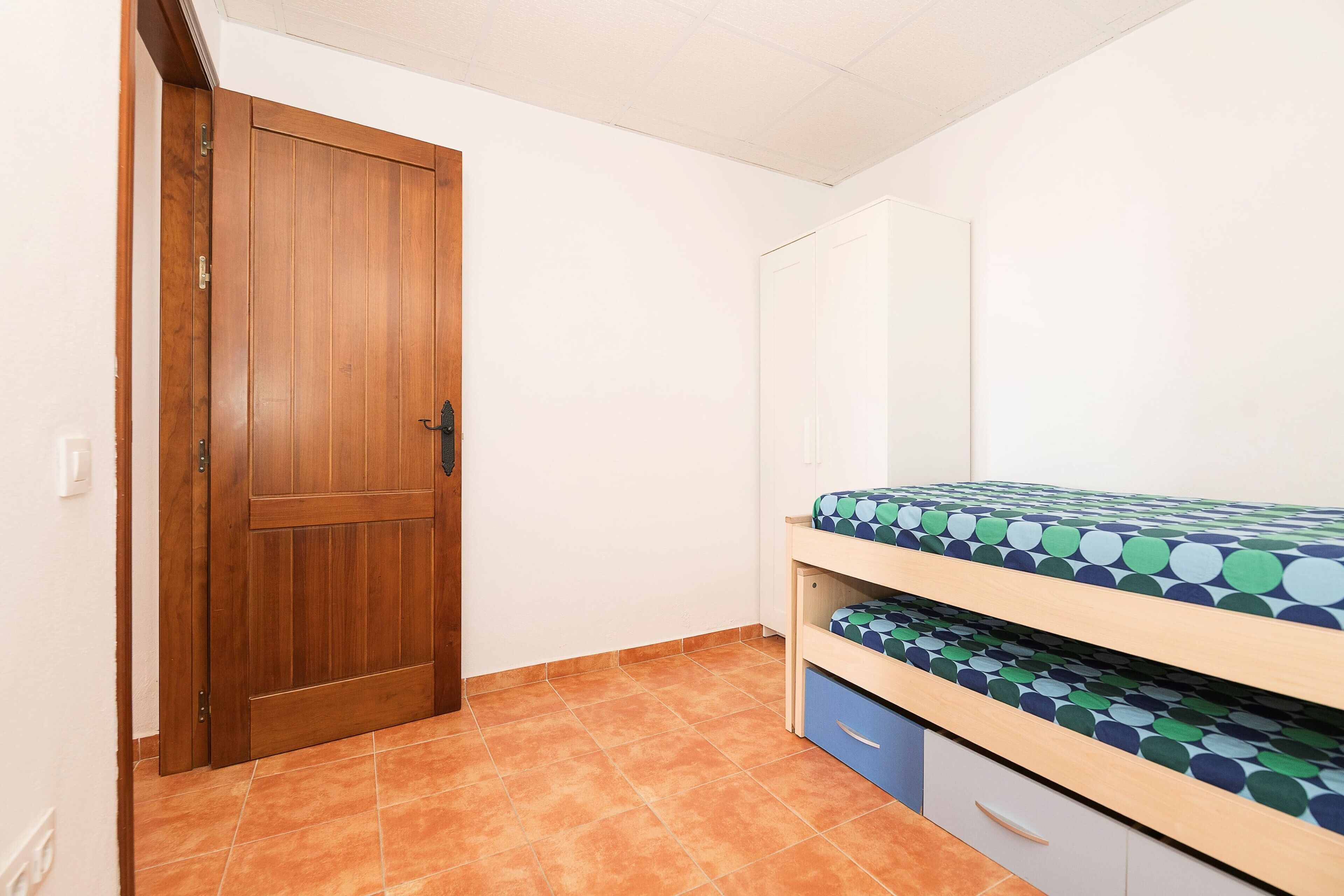 Un dormitorio con una puerta de madera, una cama con colchón estampado y un armario con cajones.
