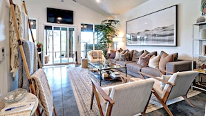 A spacious living room with a large sofa, a coffee table, and a ceiling fan. There is a large painting on the wall and a plant in the corner. - Midnight Eddy @ Water's Edge: Lake front~Hot Tub~Fire pit~Kayaks~more (Fayetteville)