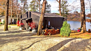 A cabin with a gravel driveway, surrounded by trees and a lake. - Midnight Eddy @ Water's Edge: Lake front~Hot Tub~Fire pit~Kayaks~more (Fayetteville)