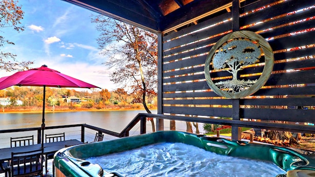 A hot tub on a wooden deck with a view of a lake and autumn trees. - Midnight Eddy @ Water's Edge: Lake front~Hot Tub~Fire pit~Kayaks~more (Fayetteville)