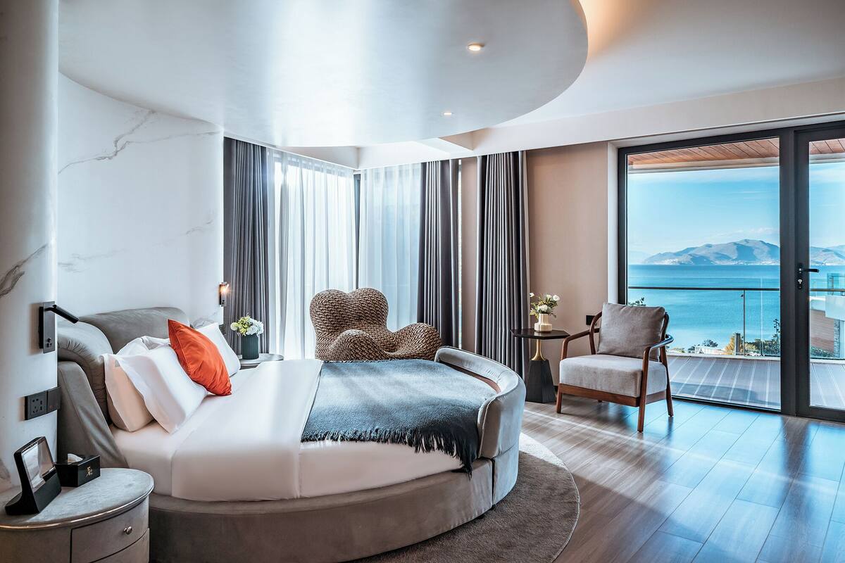 Een moderne slaapkamer met een gebogen bed, een zithoek en een balkon met uitzicht op zee.