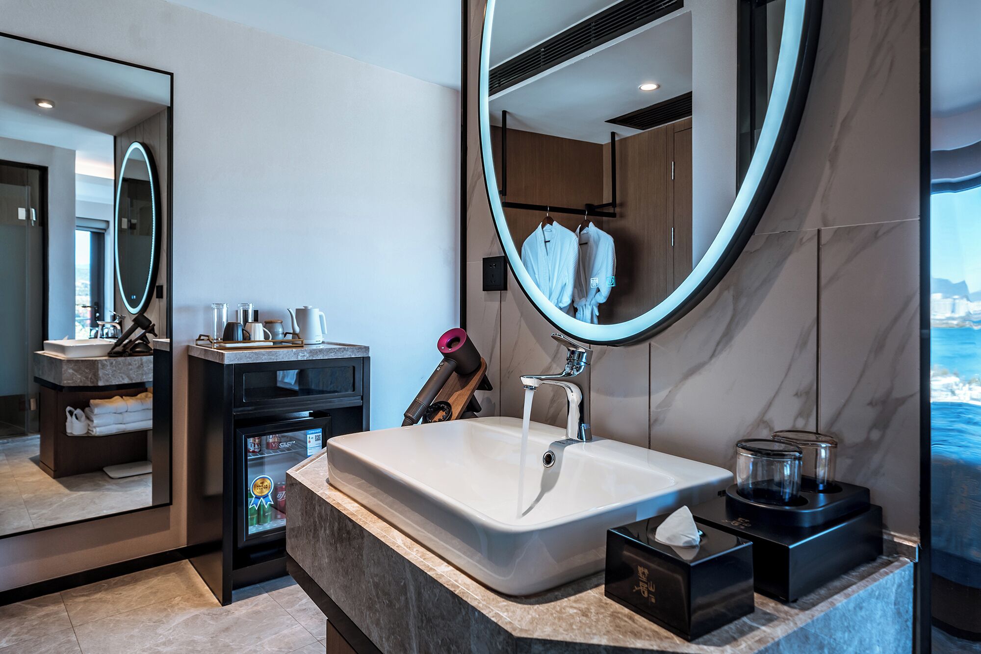 A modern bathroom with a large mirror, a bathtub, and a countertop with toiletries.
