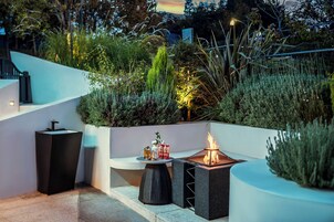 Un patio al aire libre con una chimenea, asientos y abundante vegetación.