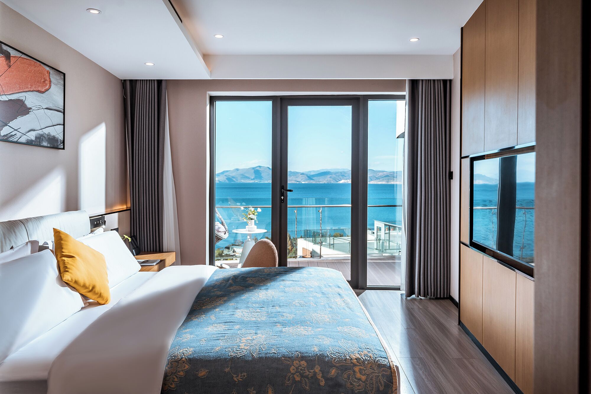 A modern hotel room with a large bed, a TV, and a balcony with a sea view.