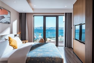 Una habitación de hotel moderna con una cama grande, televisión y balcón con vista al mar.