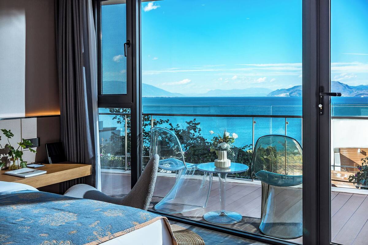 Een moderne hotelkamer met een groot balkon, een bed, een kleine tafel en een stoel.