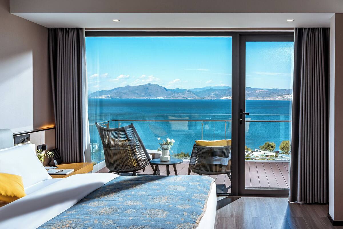 Een moderne hotelkamer met een ruim balkon, een bed, een tafeltje en een stoel.