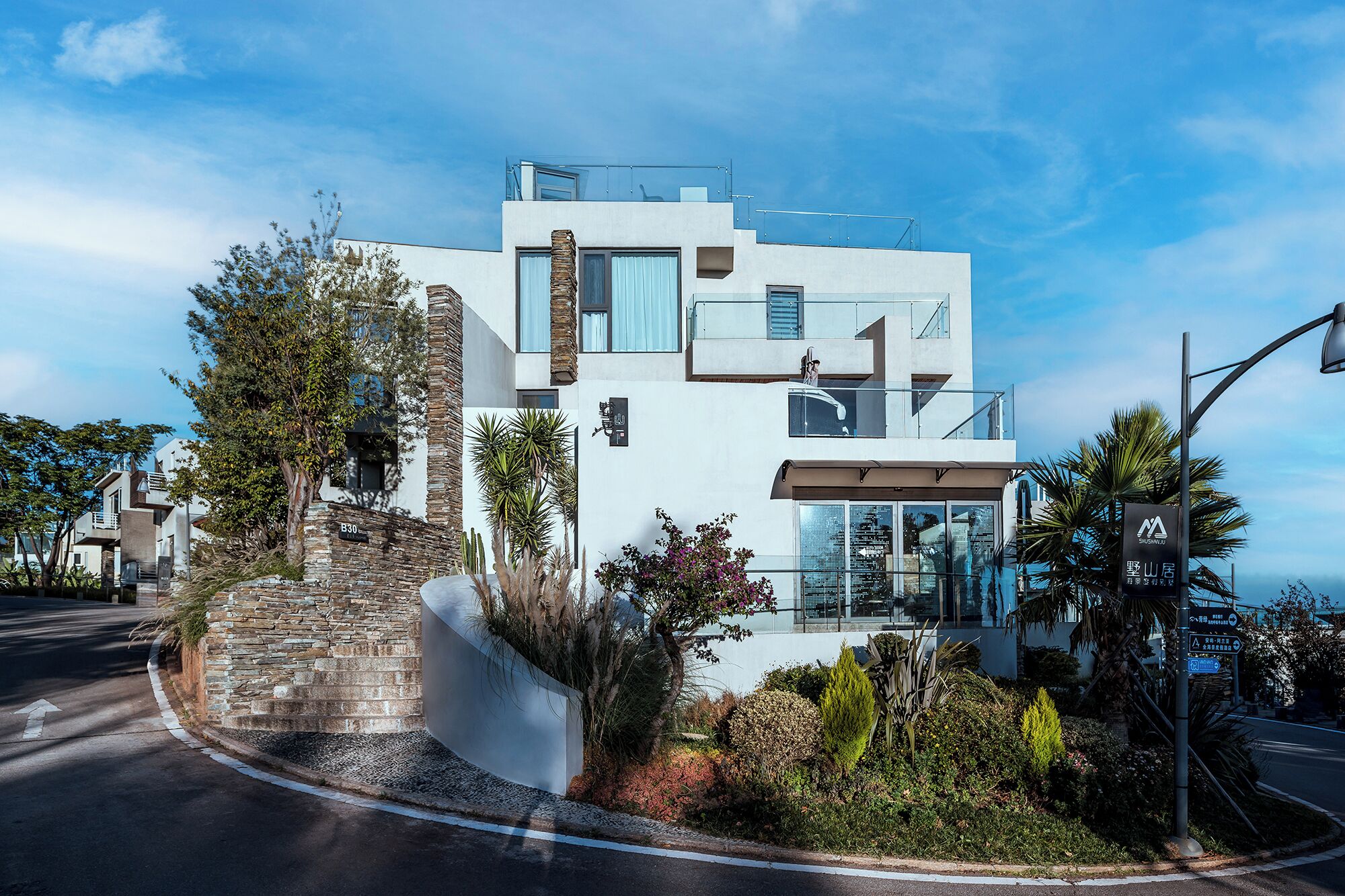 A modern two-story building with a stone facade, large windows, and a balcony.