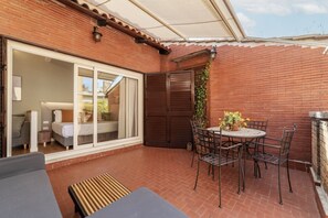 A patio with a table and chairs, a sliding glass door leading to a bedroom, and a brick wall.