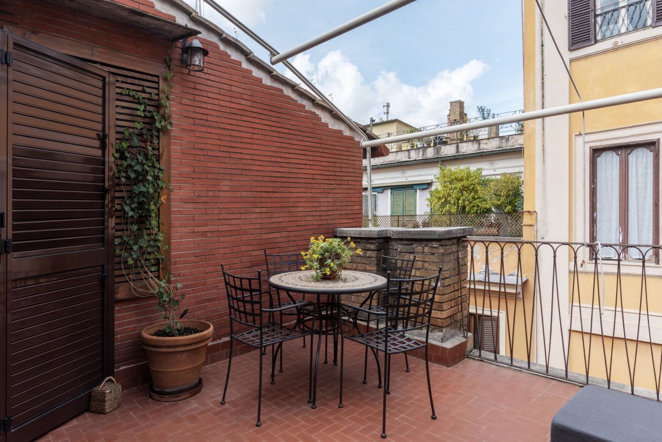 Een terras met een ronde tafel en stoelen, een bloempot en een bakstenen muur.