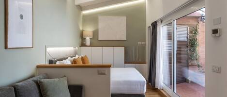 A modern, compact living space with a sofa, a bed, a small kitchenette, and a sliding glass door leading to an outdoor area.