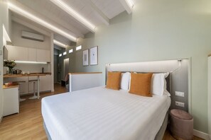 A modern hotel room with a large bed, a small kitchenette, and a bathroom visible in the background.