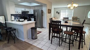A modern kitchen with white cabinets, a central island, and a dining area with a chandelier. - Birdsong Pool Retreat - Pet Friendly - 7 Min to Beach (Venice)