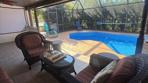 A covered patio area with wicker furniture, a pool, and a ceiling fan. - Birdsong Pool Retreat - Pet Friendly - 7 Min to Beach (Venice)