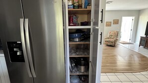 A kitchen with a stainless steel refrigerator, open pantry with shelves, and a tiled floor. - Birdsong Pool Retreat - Pet Friendly - 7 Min to Beach (Venice)
